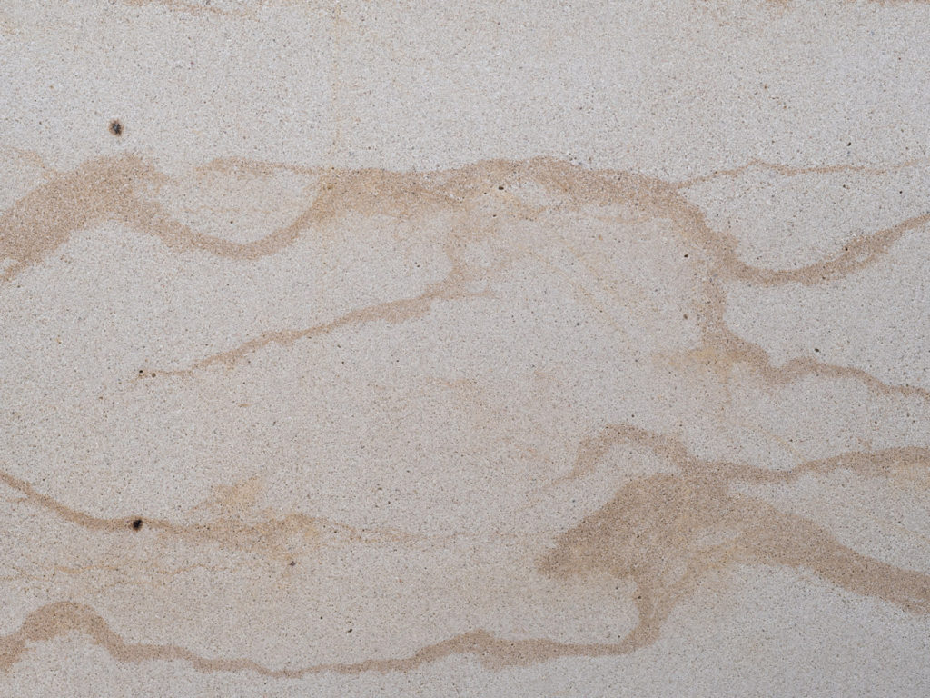 Postaer Sandstein mit subtilen, wellenförmigen braunen Linien, die horizontal darüber verlaufen. Die Textur wirkt glatt und natürlich und erinnert an geschichteten Sand oder Gestein von einem Sandsteinfeld. Vereinzelt sind ein paar kleine dunkle Flecken zu sehen.